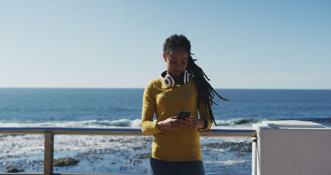 Woman Listening to Music While Checking Phone Outdoors by Ocean - Free Images, Stock Photos and Pictures on Pikwizard.com