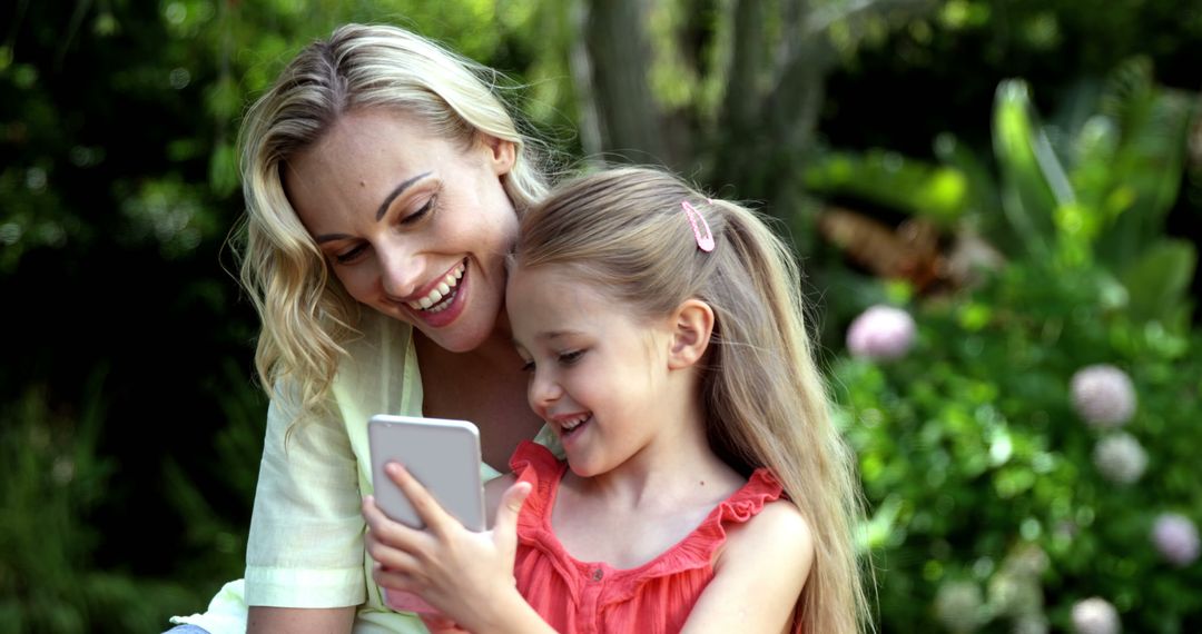 Mother and Daughter Smiling While Looking at Smartphone Outdoors - Free Images, Stock Photos and Pictures on Pikwizard.com