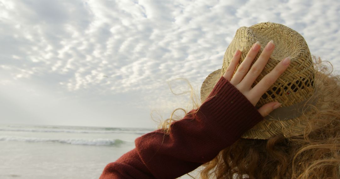 A young Caucasian woman holds onto her straw hat while looking out at the sea, with copy space - Free Images, Stock Photos and Pictures on Pikwizard.com