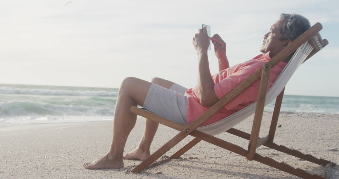 Senior Man Relaxing on Beach Using Smartphone at Sunset