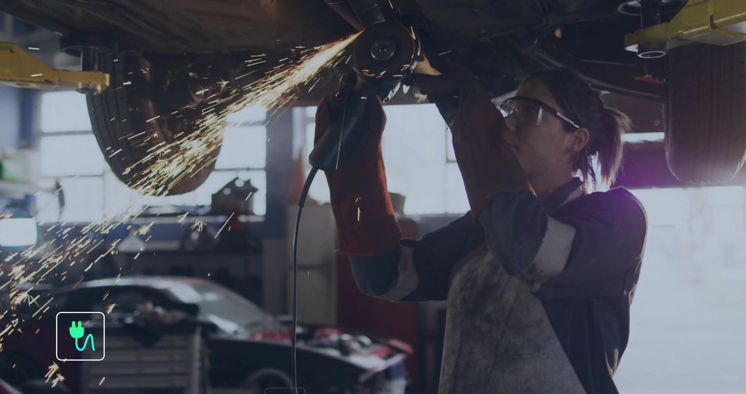 Female Mechanic Grinding Under Lifted Car Using Angle Grinder Wearing PPE in Workshop