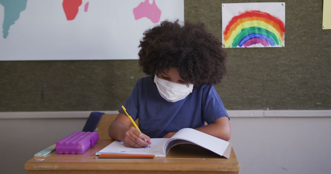 Child Wearing Face Mask Writing in Classroom Notebook