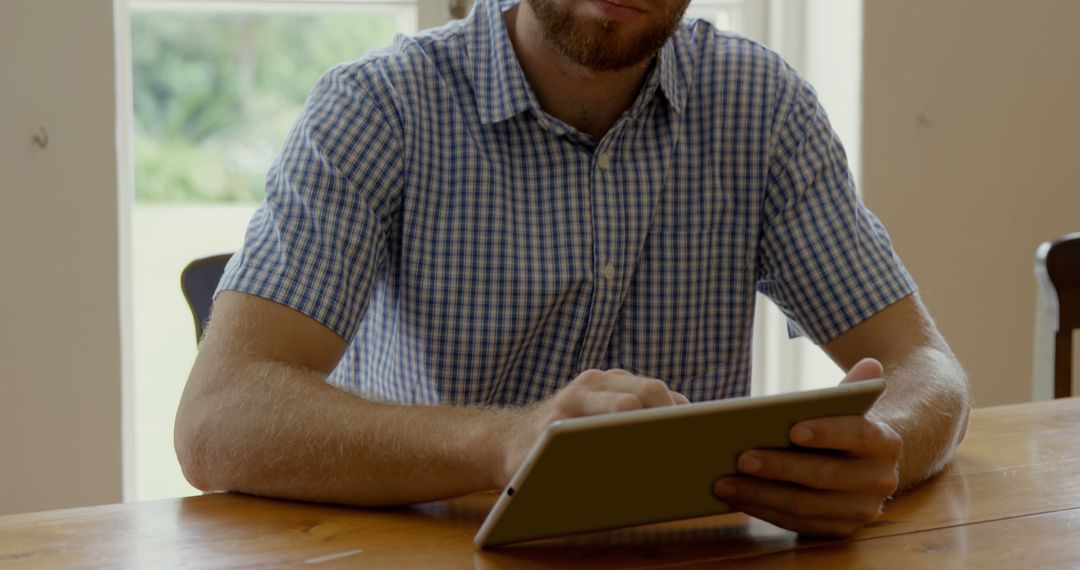 Man with Checked Shirt Using Tablet at Wooden Table - Free Images, Stock Photos and Pictures on Pikwizard.com