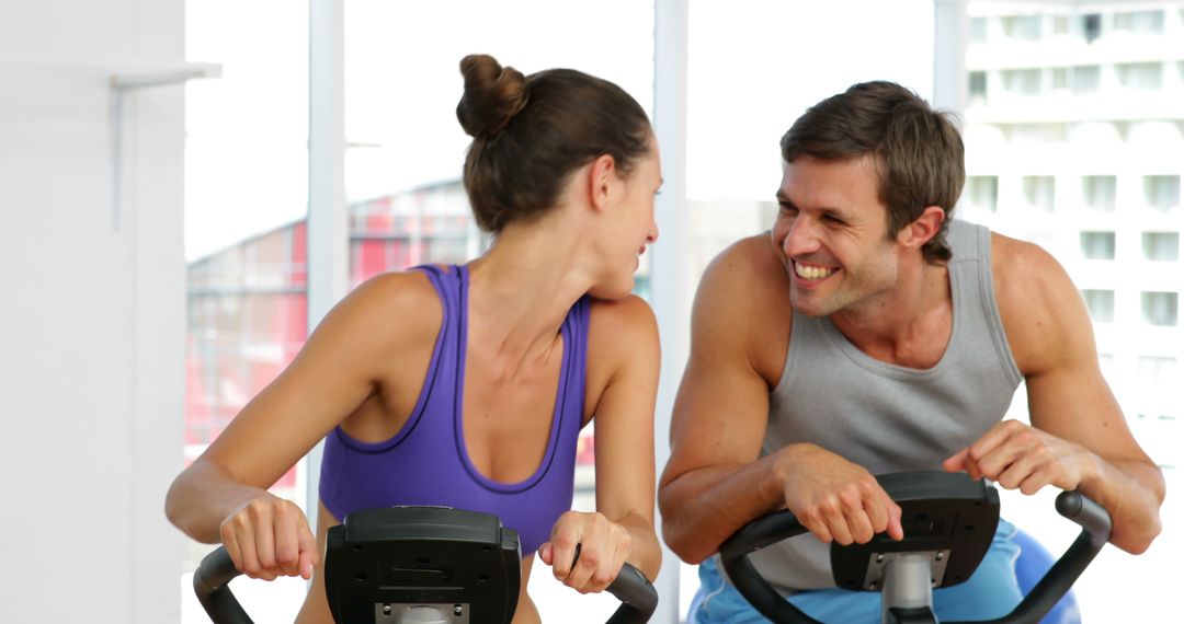 Couple Enjoying Exercise Bikes Together At Gym