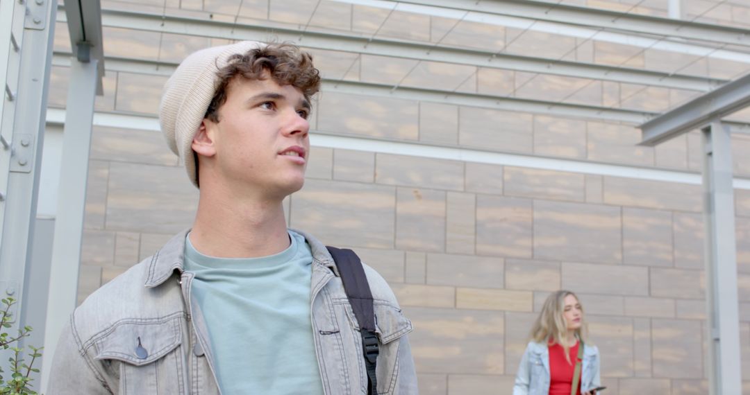 Young man exploring modern urban plaza wearing beanie and denim jacket