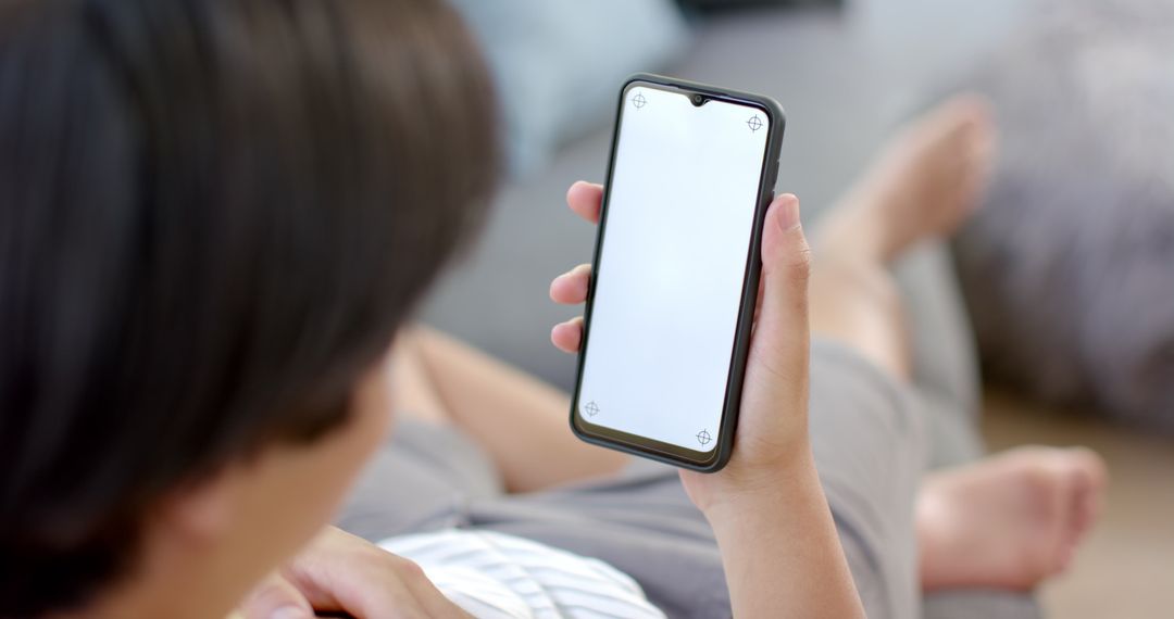 Young Asian Man Relaxing at Home Holding Smartphone with Blank Screen