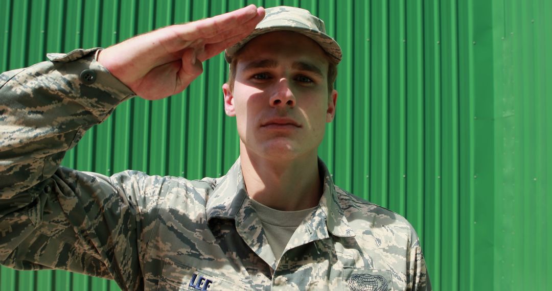 Soldier in Fatigues Giving a Salute in Front of Green Wall - Free Images, Stock Photos and Pictures on Pikwizard.com