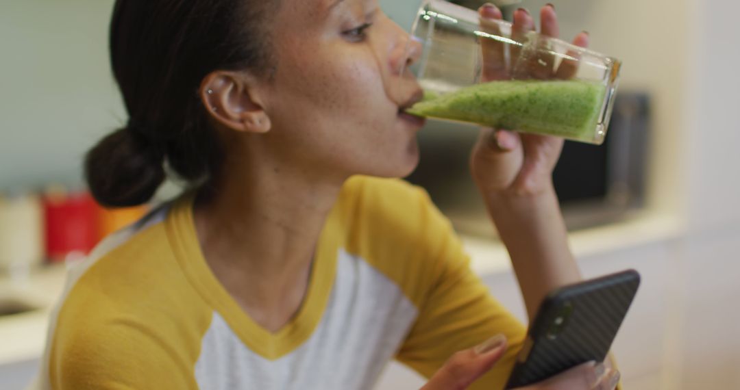 Woman Drinking Green Smoothie while Using Smartphone in Kitchen - Free Images, Stock Photos and Pictures on Pikwizard.com