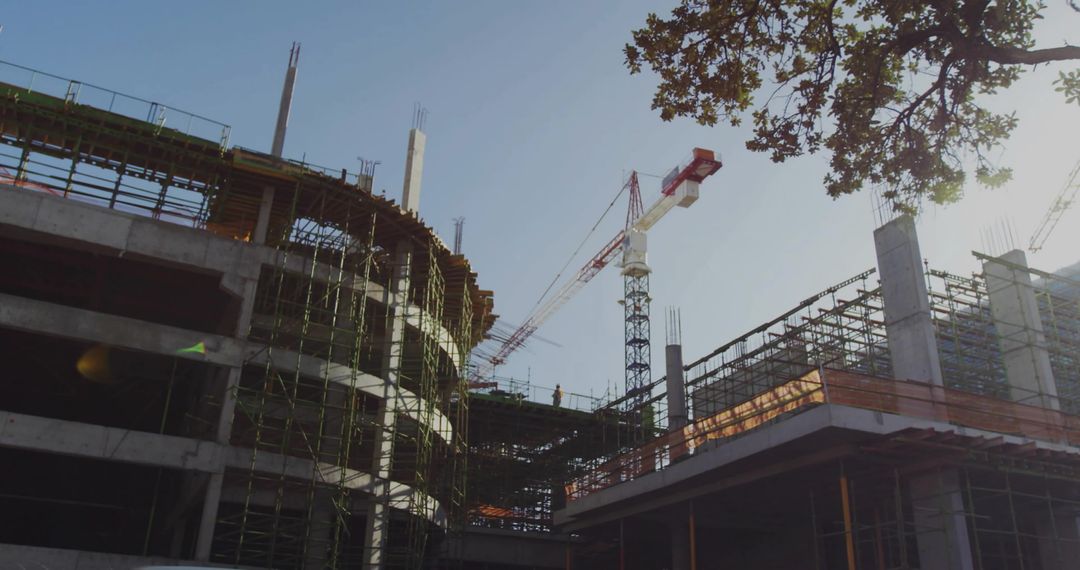 Constructing curved concrete building with scaffolding and tower cranes in urban daylight
