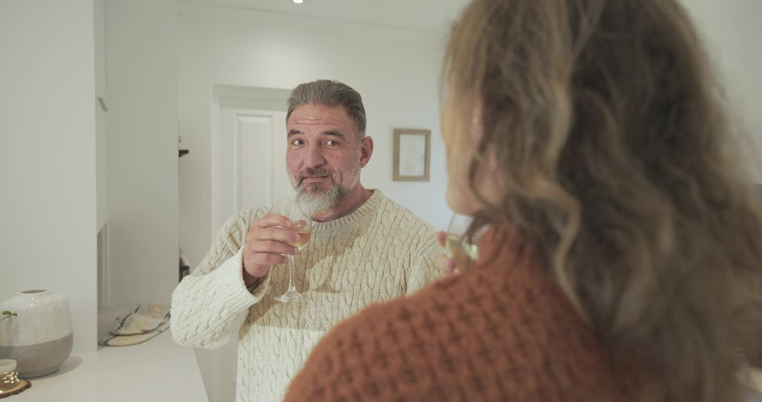 Senior Man Enjoying Wine Conversation with Middle-Aged Woman at Kitchen Counter