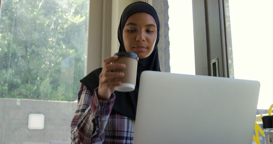 Young Woman in Hijab Working on Laptop Drinking Coffee - Free Images, Stock Photos and Pictures on Pikwizard.com