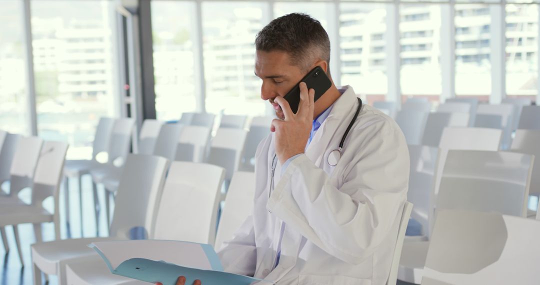 Doctor Holding Medical Files While Talking on Phone in Modern Conference Room - Free Images, Stock Photos and Pictures on Pikwizard.com