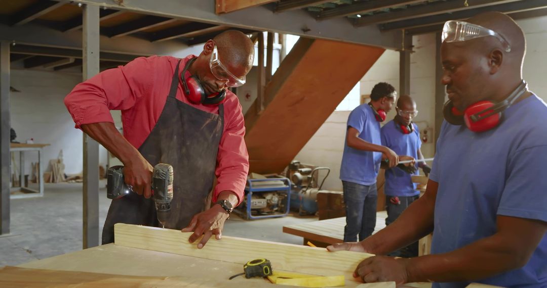 Carpenter Drilling Wooden Plank in Workshop While Teammates Measuring and Cutting