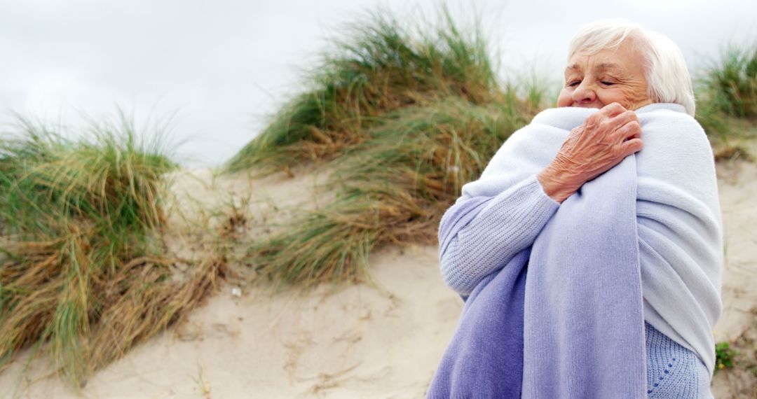 Senior Woman Wrapped in Blanket on Beach Dunes on Cloudy Day - Free Images, Stock Photos and Pictures on Pikwizard.com