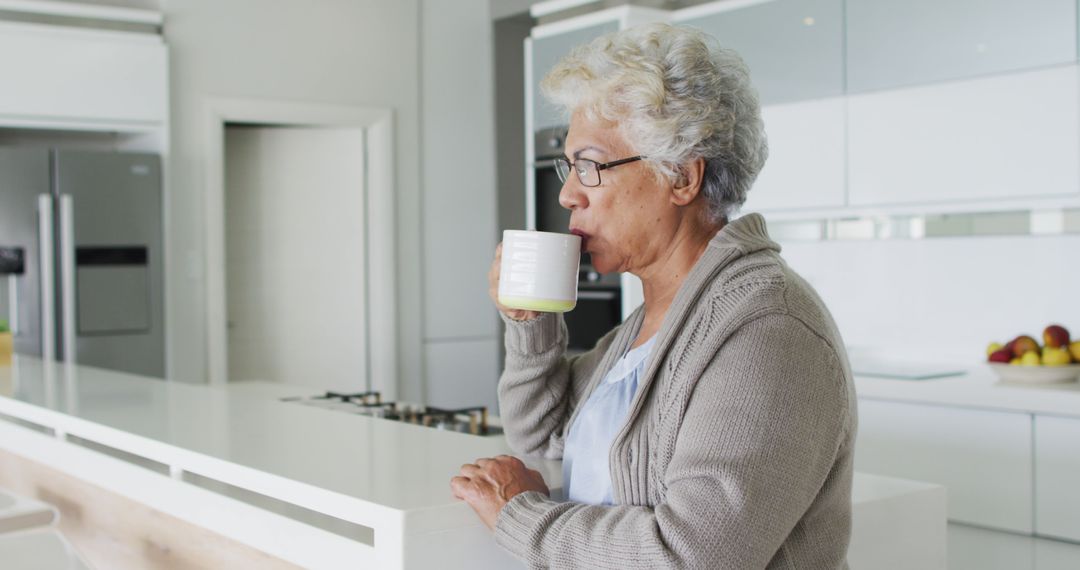 Senior woman sipping coffee in modern kitchen - Free Images, Stock Photos and Pictures on Pikwizard.com