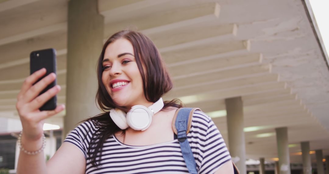 Smiling Young Woman with Headphones Taking Selfie Outdoors - Free Images, Stock Photos and Pictures on Pikwizard.com