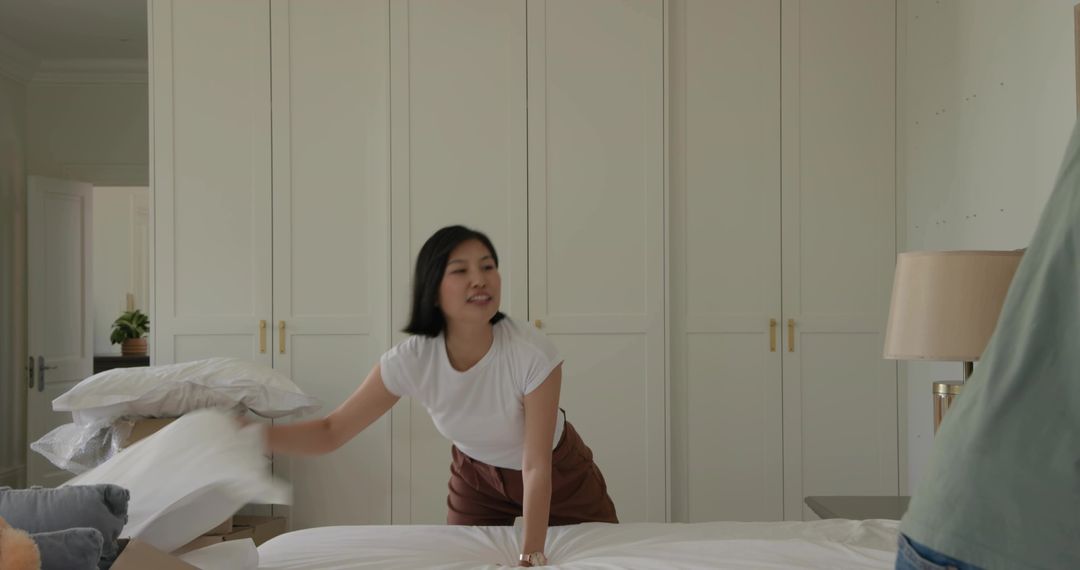 Woman Making Bed in Minimalist Bedroom with Wardrobes and Neutral Linens, Morning Routine
