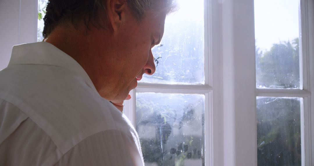 Pensive man standing by bright window - Free Images, Stock Photos and Pictures on Pikwizard.com