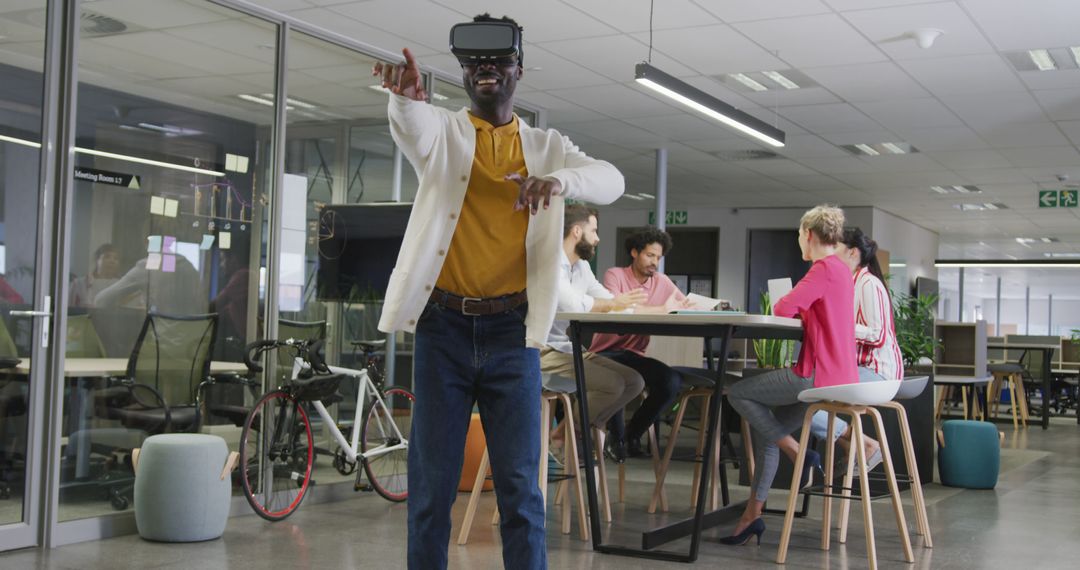 Happy african american businessman using vr headset over colleagues in office - Free Images, Stock Photos and Pictures on Pikwizard.com