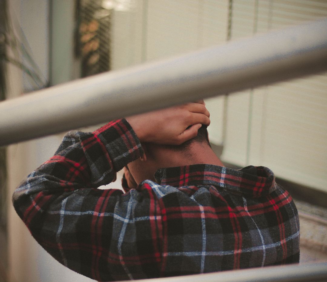 Young Man in Plaid Shirt Holding Head in Stressful Moment - Free Images, Stock Photos and Pictures on Pikwizard.com