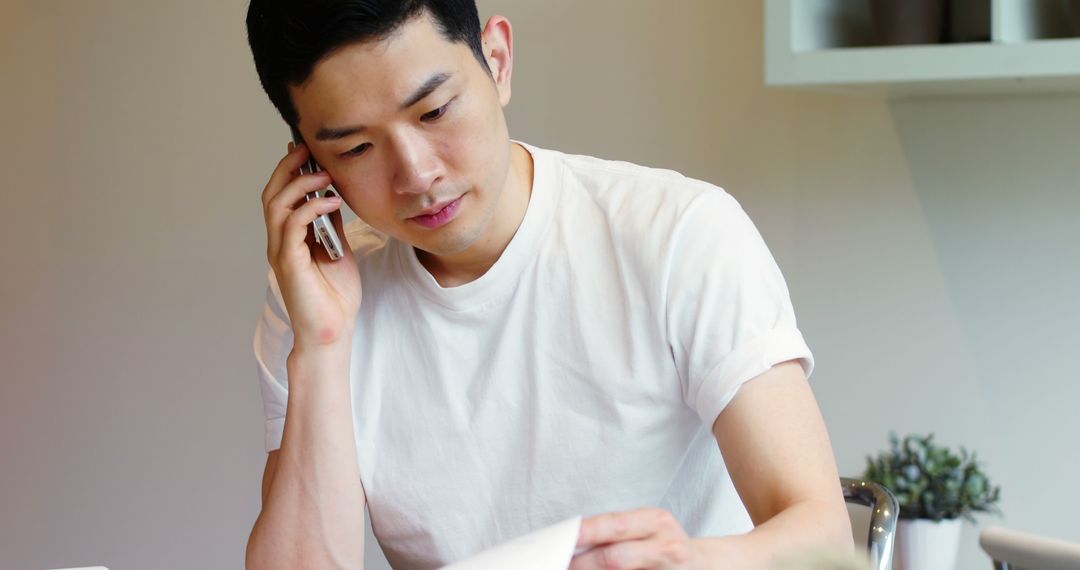 Young Man Talking on Phone While Reviewing Documents at Home - Free Images, Stock Photos and Pictures on Pikwizard.com