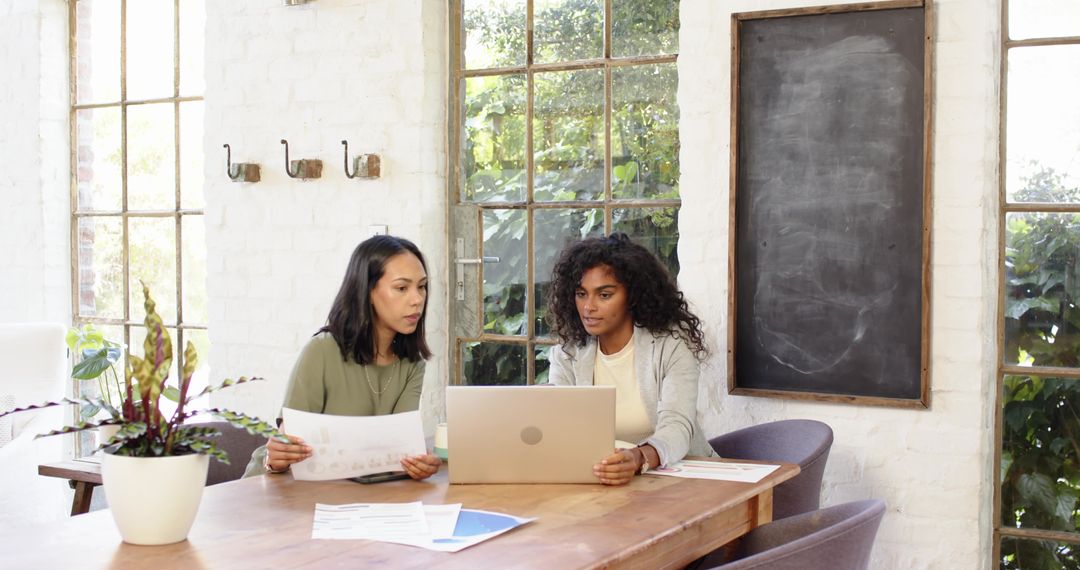 Female Professionals Collaborating with Charts and Laptop in Modern Office