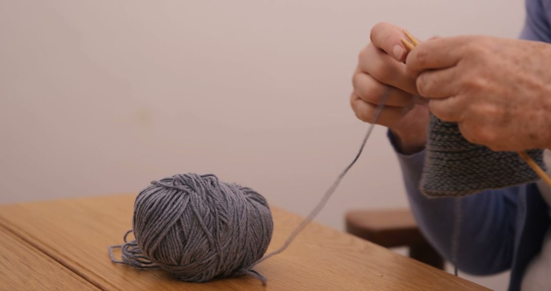 Senior hands knitting grey wool with wooden needles at wooden table - Free Images, Stock Photos and Pictures on Pikwizard.com