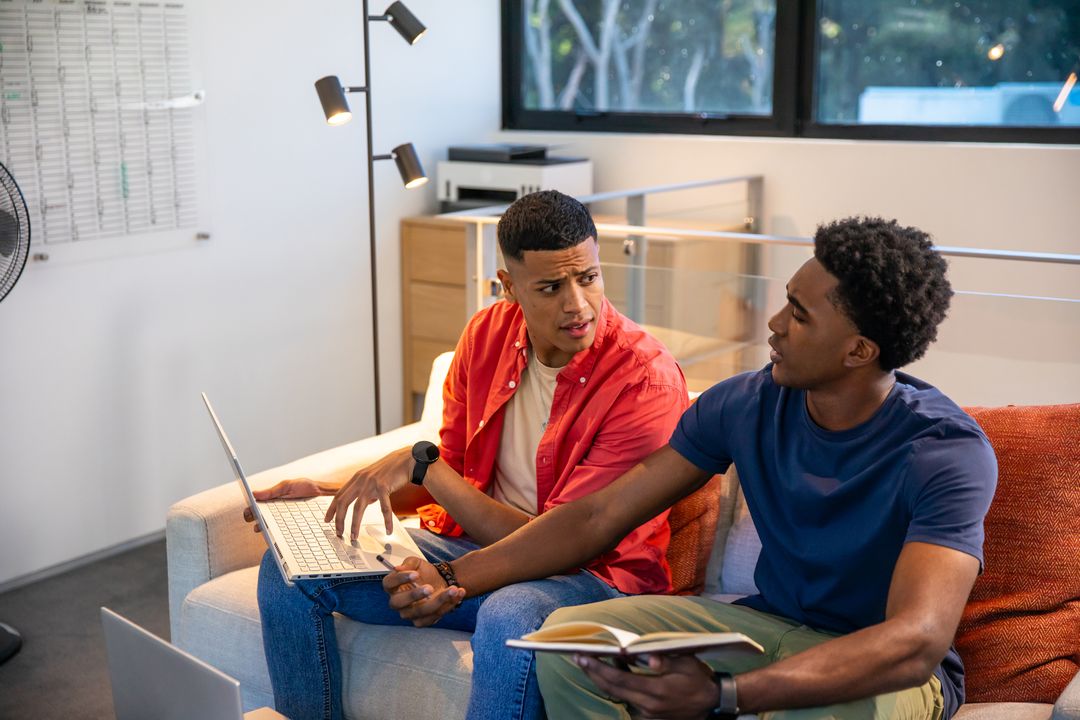 Colleagues Engaged in Discussion Using Laptop and Book in Office Lounge