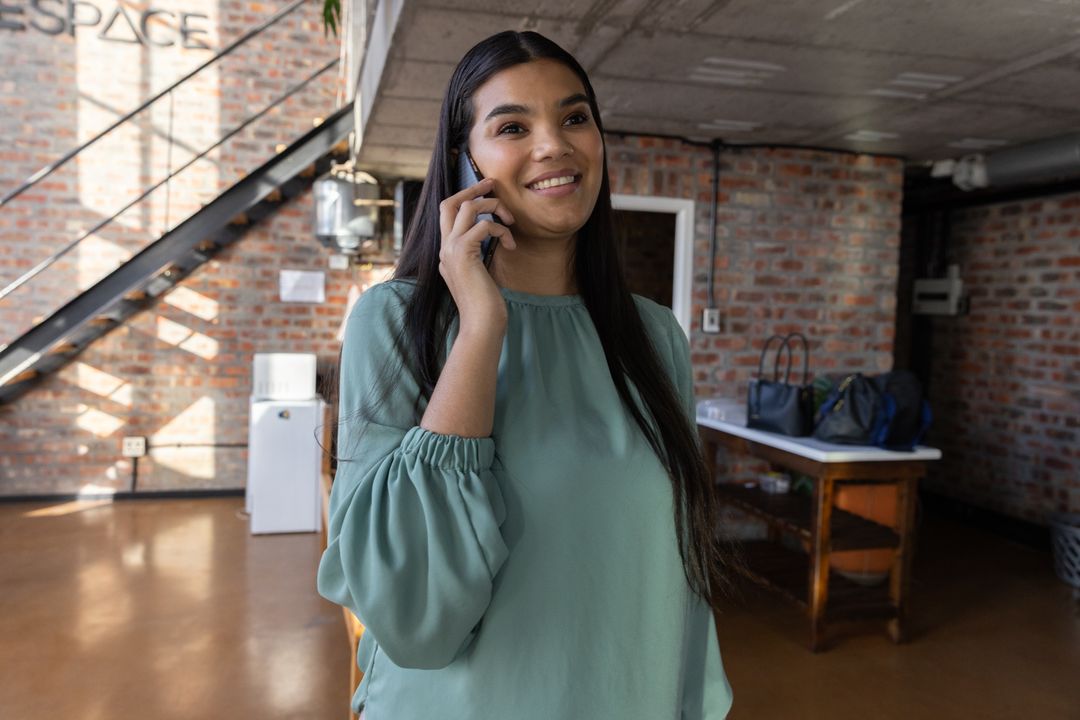Smiling Woman Engaged in Phone Conversation in Loft-Style Office