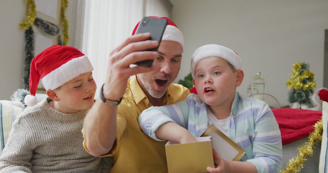 Caucasian father and two sons opening gifts while having a imagecall on smartphone during christmas - Free Images, Stock Photos and Pictures on Pikwizard.com