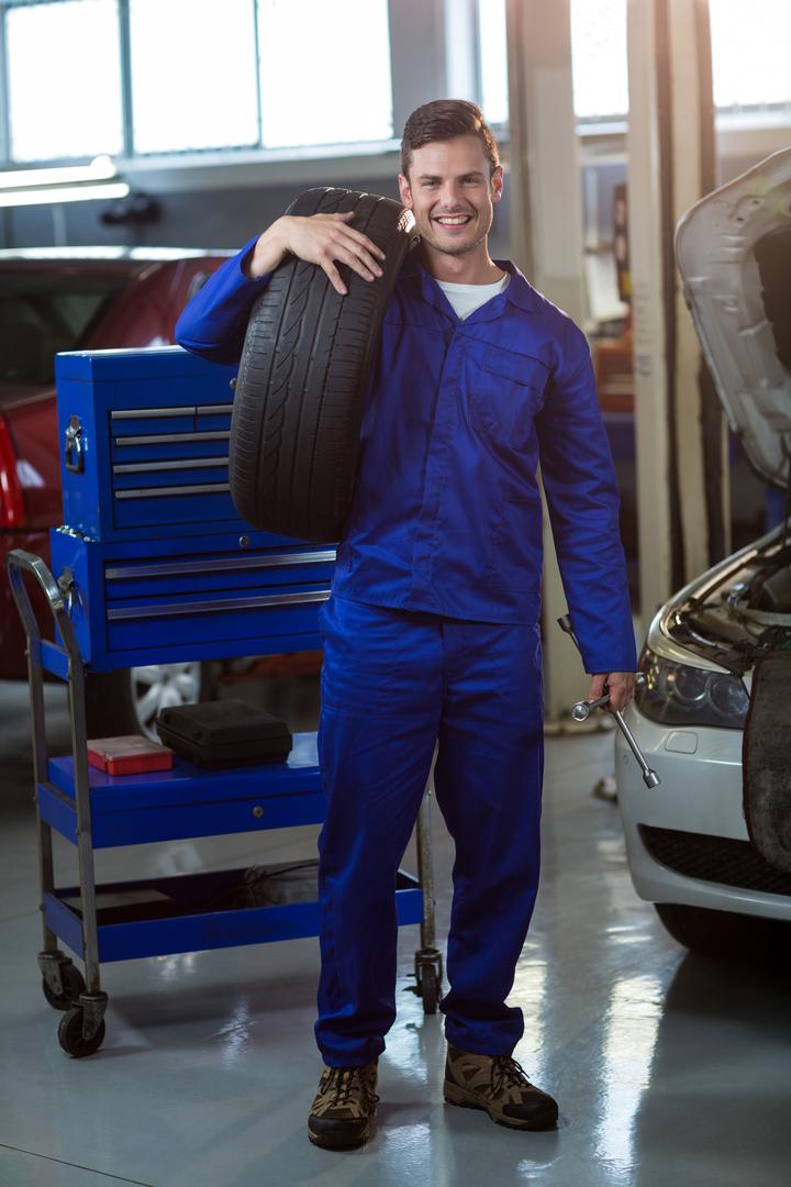 Portrait of mechanic carrying a tyre - Free Images, Stock Photos and Pictures on Pikwizard.com