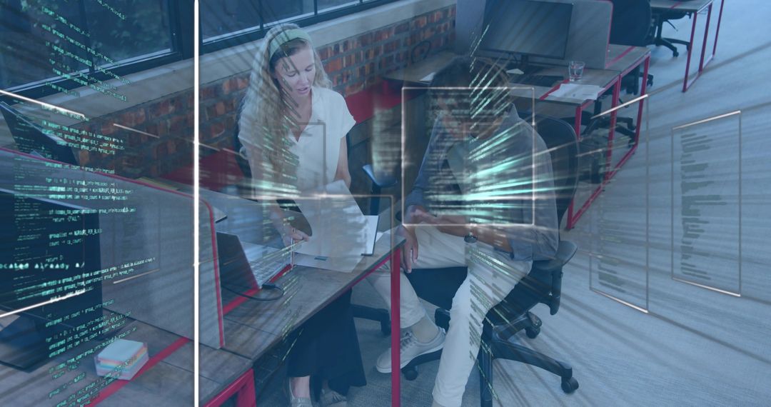 Collaborating professionals reviewing code at open-plan office desk with laptop tablet