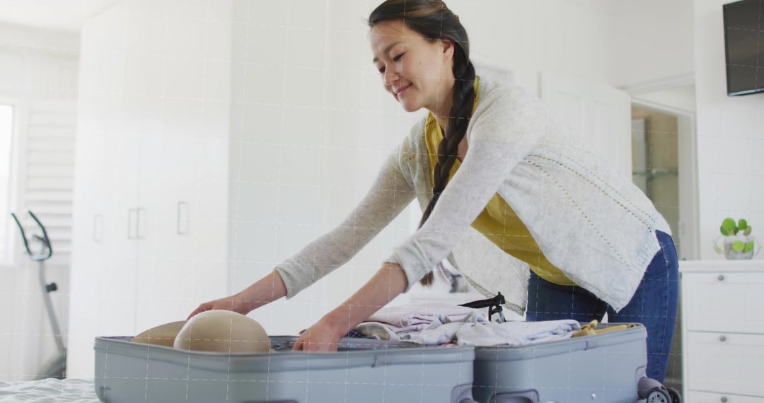 Mid-adult Korean woman packing suitcase in bright modern bedroom preparing for travel