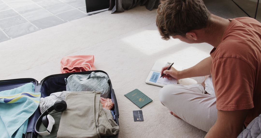 Young man packing suitcase and planning trip with passport, checklist, headphones