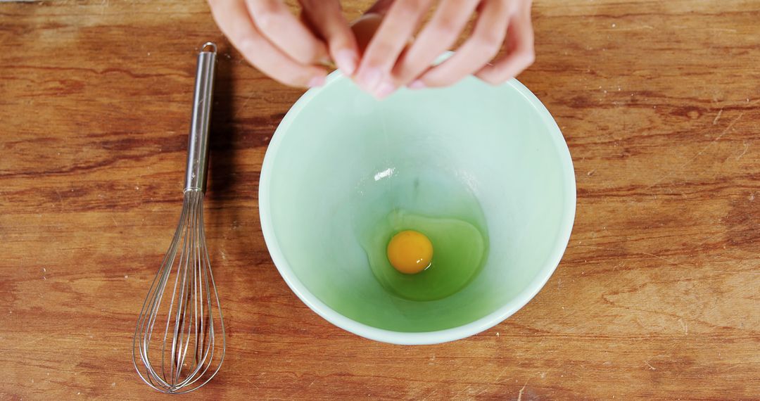 Person Cracking Egg into Mixing Bowl on Wooden Surface - Free Images, Stock Photos and Pictures on Pikwizard.com