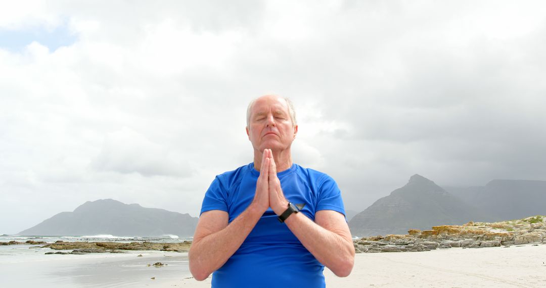 Senior Man Meditating on Beach with Mountains in Background - Free Images, Stock Photos and Pictures on Pikwizard.com