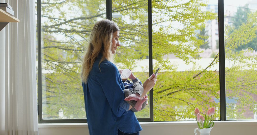 Mother Holding Baby While Using Smartphone in Bright Living Room - Free Images, Stock Photos and Pictures on Pikwizard.com