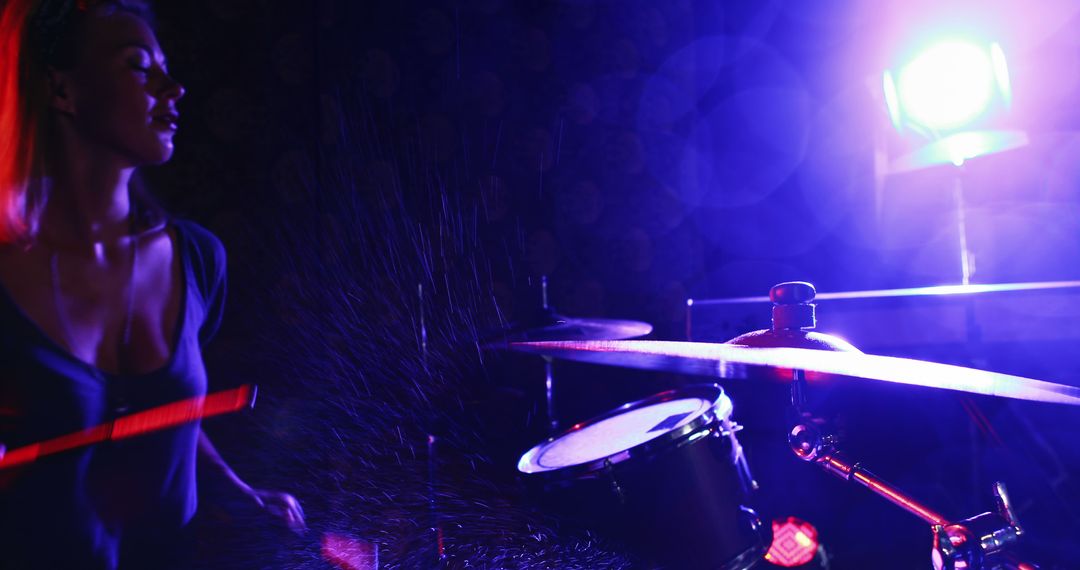 A young woman delivers a dynamic drumming performance under dramatic stage lights. - Free Images, Stock Photos and Pictures on Pikwizard.com