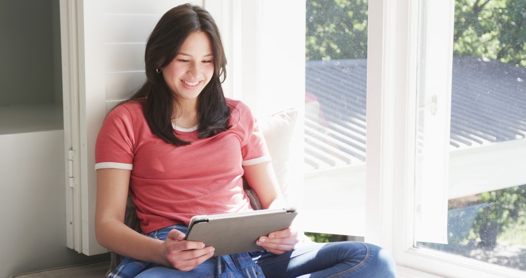 Young Woman Smiling and Using Tablet by Window - Free Images, Stock Photos and Pictures on Pikwizard.com