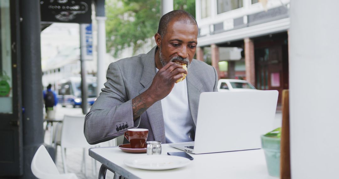 Businessman Eating Sandwich While Working on Laptop at Outdoor Café - Free Images, Stock Photos and Pictures on Pikwizard.com