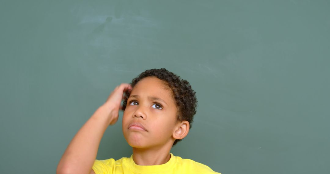 Thoughtful Schoolboy Scratching Head in Front of Blackboard