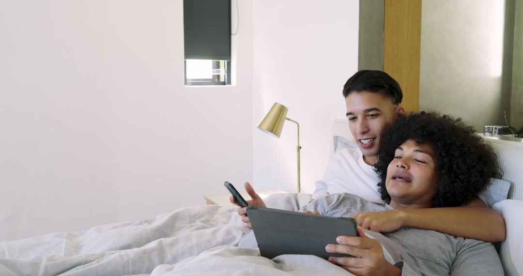 Happy Couple Relaxing in Bed Sharing Digital Devices