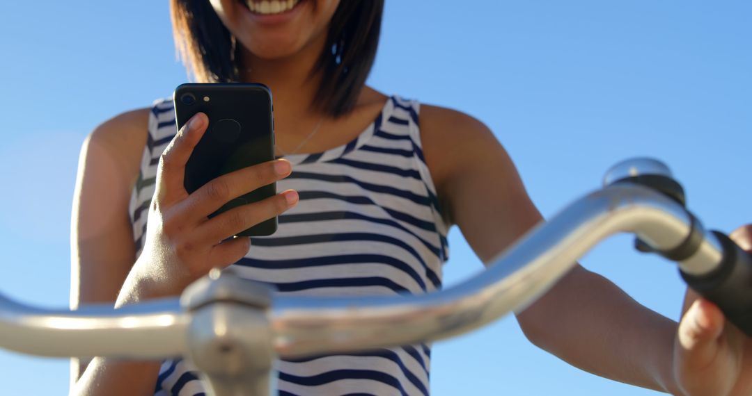 Woman Checking Smartphone While Holding Bicycle Handlebar on Clear Day - Free Images, Stock Photos and Pictures on Pikwizard.com