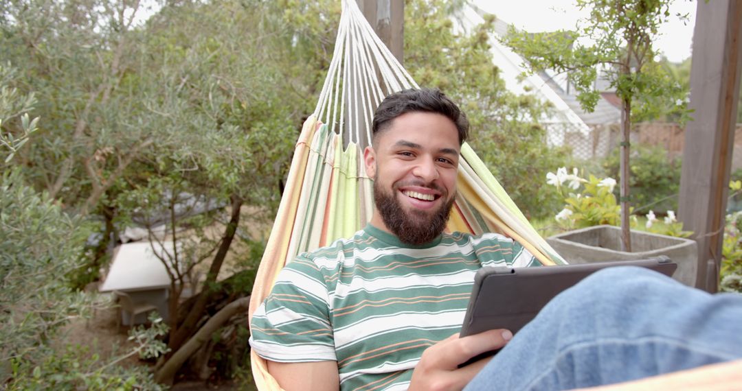 Smiling Man Relaxing in Hammock Outdoors with Tablet