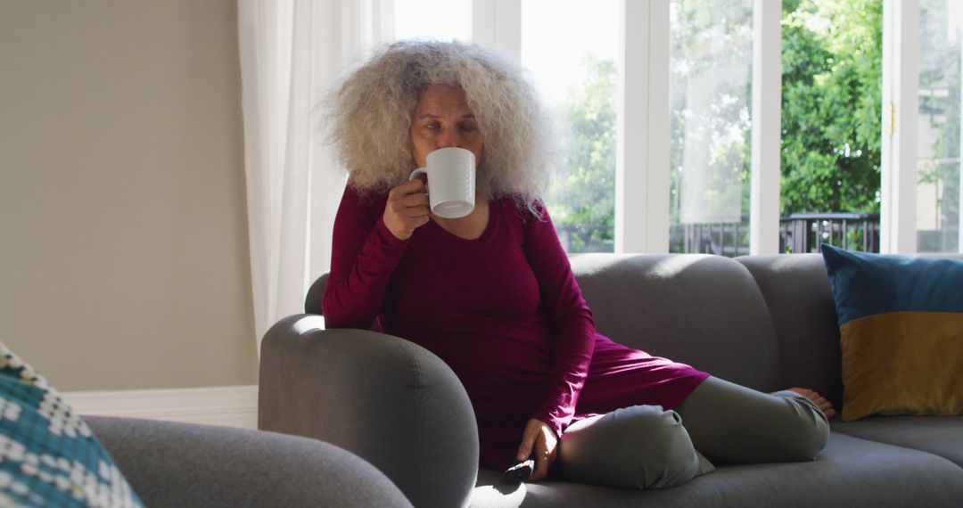 Senior Woman Relaxing On Couch While Drinking Coffee In Bright Living Room - Free Images, Stock Photos and Pictures on Pikwizard.com