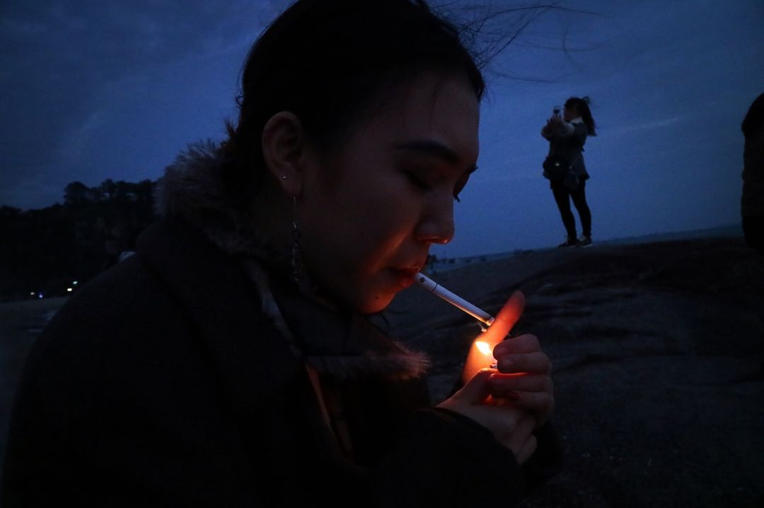 Young Woman Lighting Cigarette at Dusk on Beach - Free Images, Stock Photos and Pictures on Pikwizard.com