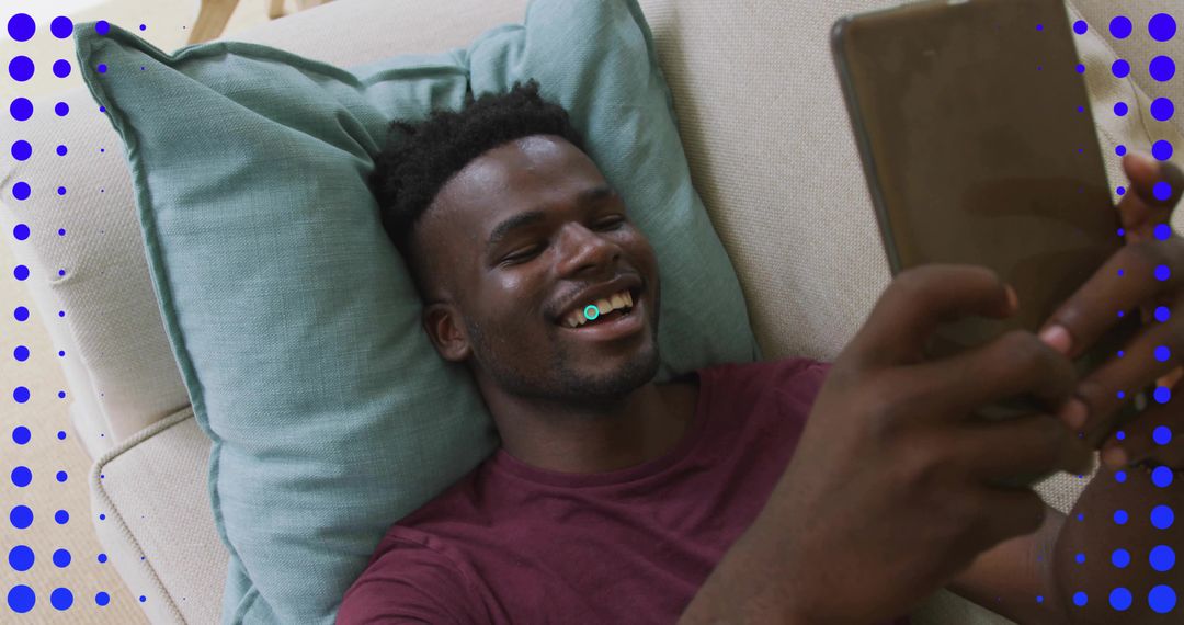 Smiling man relaxing on sofa using tablet for streaming, browsing, and video chat