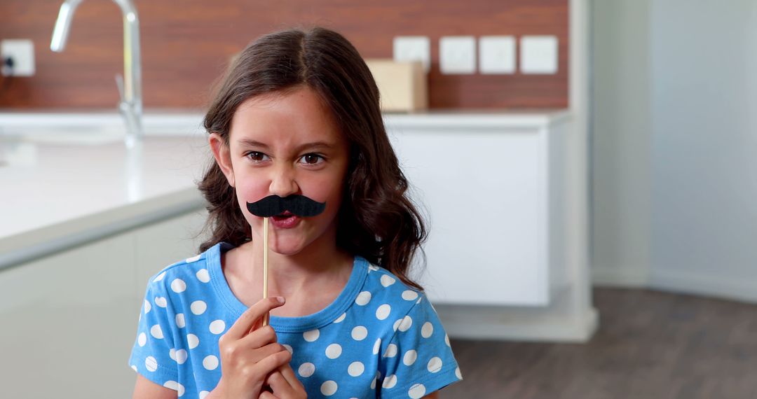 Girl Holding Fake Mustache Prop in Modern Kitchen - Free Images, Stock Photos and Pictures on Pikwizard.com