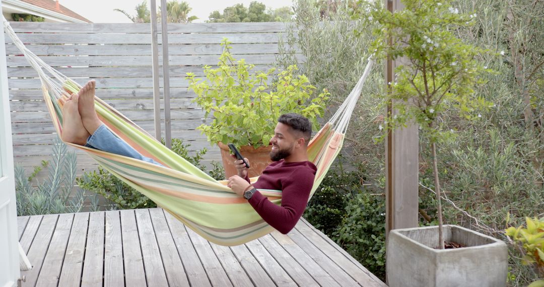 Relaxed Man Enjoying Hammock on Sunny Deck with Smartphone