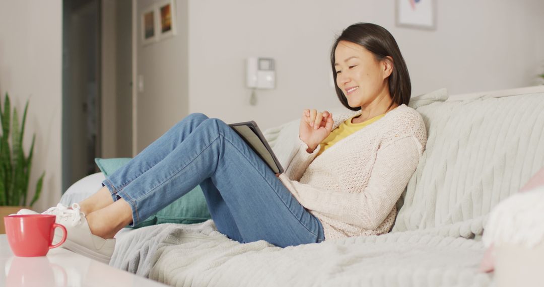 Happy Asian Woman Relaxing on Sofa with Tablet - Free Images, Stock Photos and Pictures on Pikwizard.com